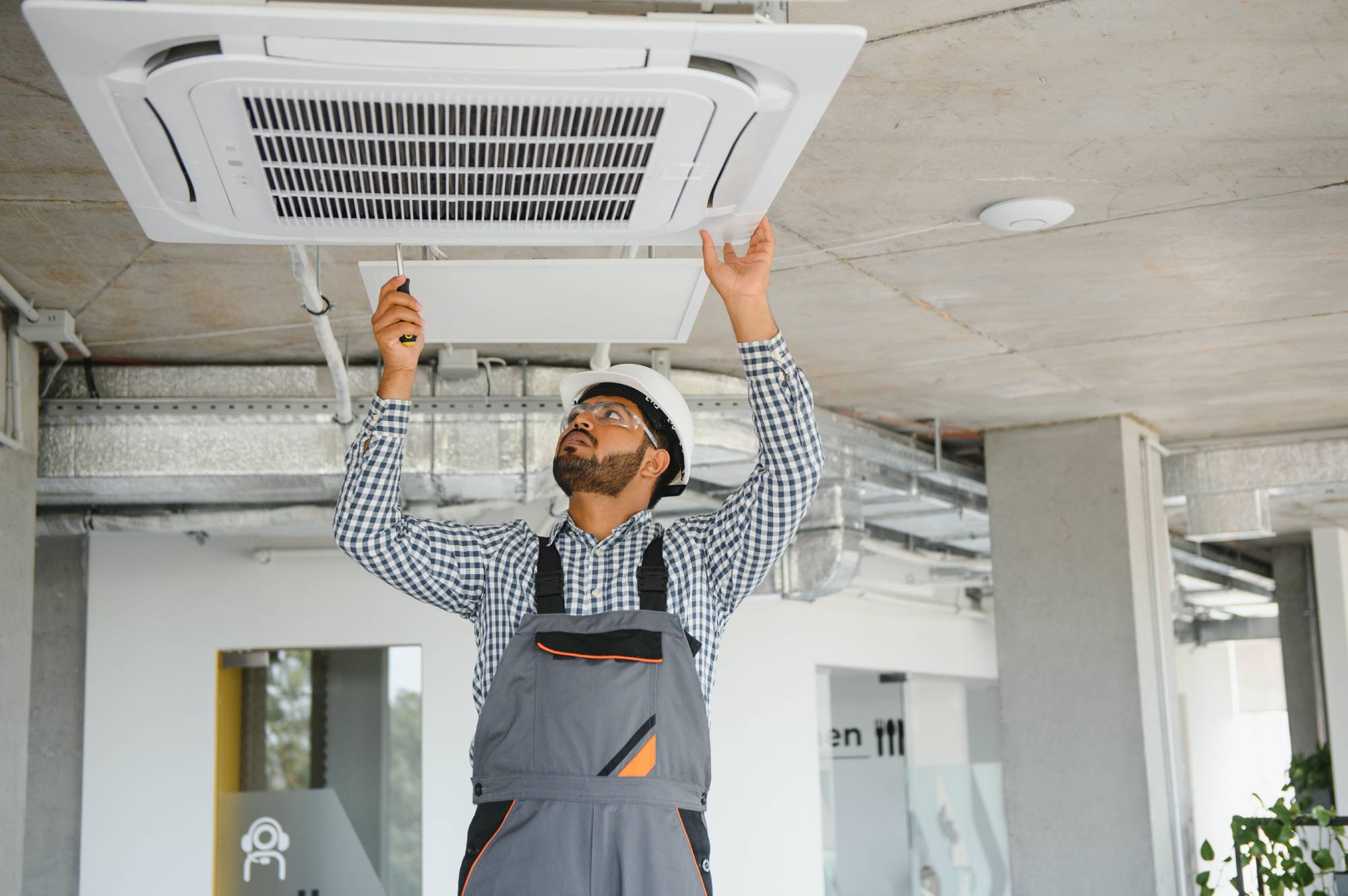 Technician installing an air conditioning unit onto an office ceiling